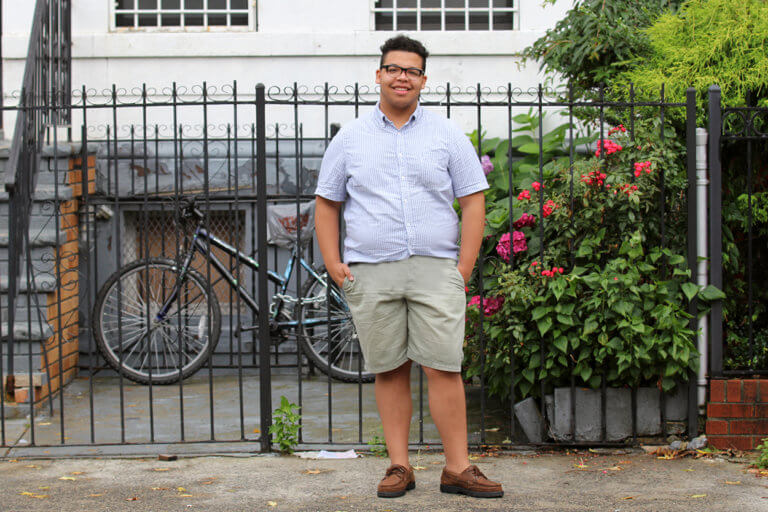 Young man standing on a street with hands in pockets, looking into the camera