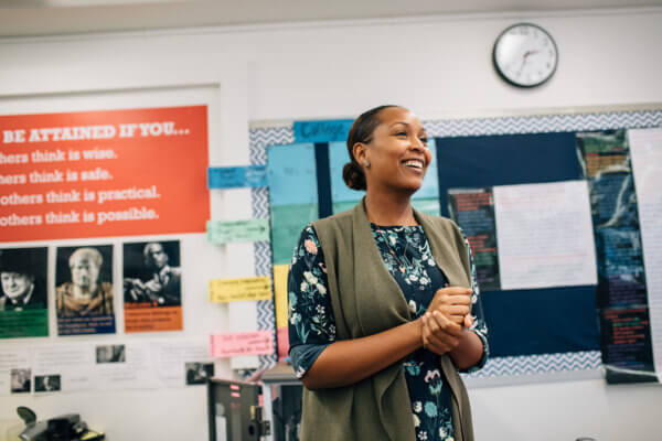 Teacher smiling at the front of her classroom — reference photo from achievementfirst.org