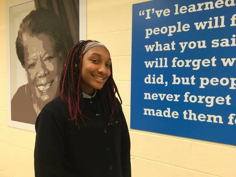 A student stands with a poster of Maya Angelou